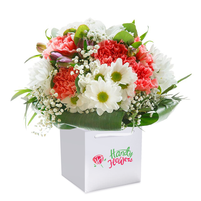 A masterful combination of garden-fresh flowers is captured in this arrangement, perfectly suited for the discerning residents of Hillingdon. Displayed proudly in a sleek white square gift bag, the bouquet features generous clusters of coral and soft peach carnations, each bloom deeply ruffled and vibrant, radiating cheer within the composition. Intertwined among the centrepieces are luminous white daisies, each displaying a golden-green eye, their tidy petals echoing the essence of springtime enjoyed in the green spaces of Hillingdon and Hayes. Ethereal baby's breath winds lightly around the central blooms, adding a weightless texture like cool morning air. Purple-tinged buds, quietly nestled among the flowers, offer subtle hints of what's yet to come, their presence deepening the overall palette. The surrounding deep green foliage is arranged with precision, broad, shiny leaves creating a supportive frame, much like the tranquil borders of Stockley Park. The gift bag's thick white ribbon handles offer secure and stylish transport, positioned so the arrangement feels ready for an effortless handover or doorstep delivery. The clear, undistracted white background ensures every vibrant shade and elegant line stands out. This bouquet from Florist Hillingdon beautifully fuses artistry, freshness, and thoughtful presentation, making it an ideal choice for birthdays, welcoming gestures, or sharing heartfelt moments anywhere from Ickenham to Cowley.